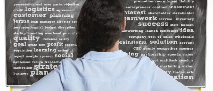 Woman in blue shirt with back to camera looks at chalkboard with lots of business relevant words on it