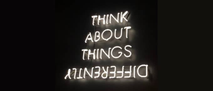 White neon sign on black background with message "think about things differently"