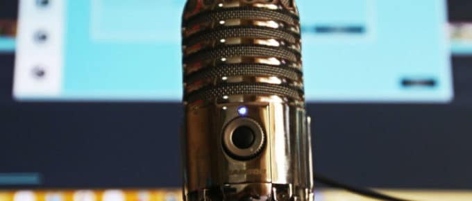 Close up on a podcast interview microphone with a computer screen in the background, out of focus